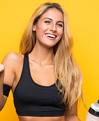 A young woman holding a bottle of water on a yellow background.